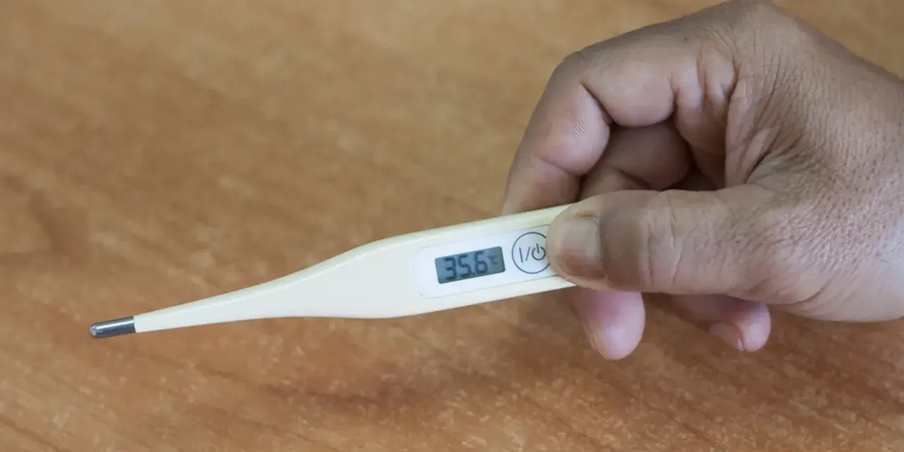 Dłoń trzyma termometr wskazujący 35.6°C. To oznaka obniżona temperatura.