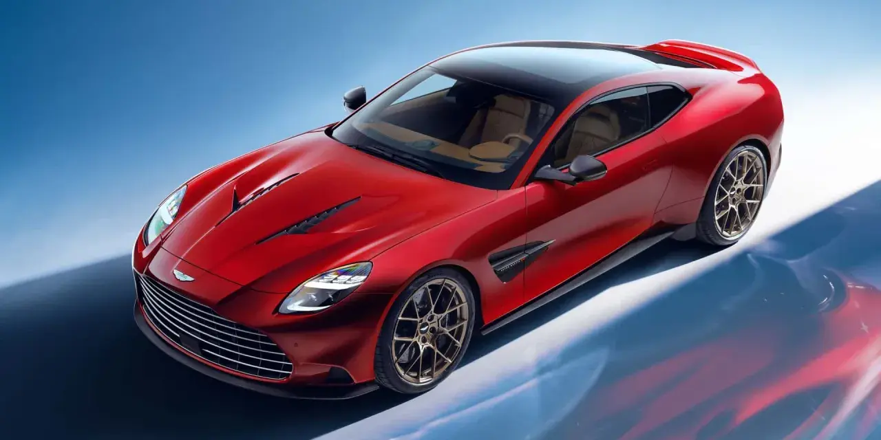 Czerwony Aston Martin Vanquish z brązowym wnętrzem i czarnym dachem, prezentujący swoje sportowe linie na tle błękitnego nieba.