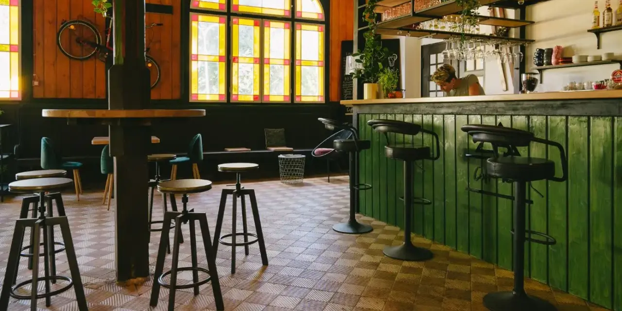 Wnętrze kawiarni z zielonym barem, stołkami i rowerem na ścianie. Idealne miejsce na coffee ride.