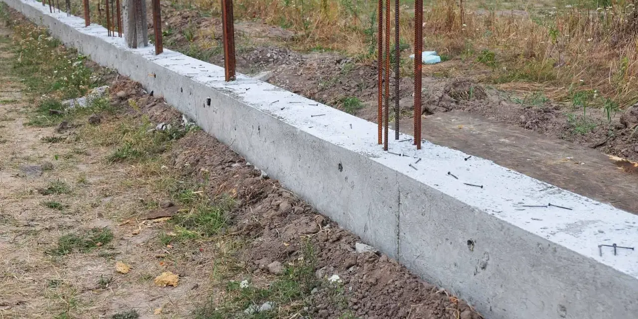 Zbrojony fundament czeka na wylewanie betonu. Widać stalowe pręty wystające z betonowej ławy fundamentowej.