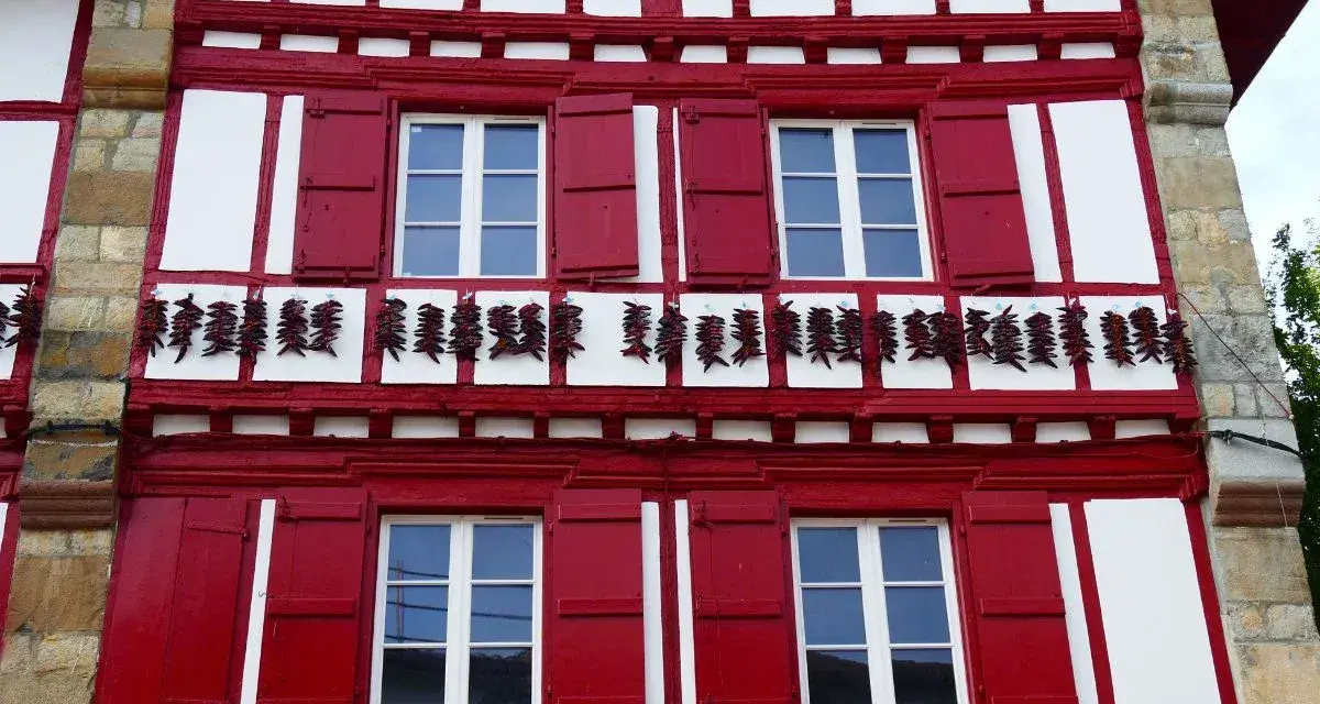 Façade rouge et blanche typique d'Espelette, avec des piments séchant. Combien de temps pour visiter Espelette ? Une journée suffit pour admirer ce village pittoresque.
