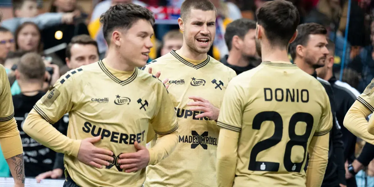 Piłkarze ręczni Górnika Zabrze w złotych strojach rozmawiają na boisku.
