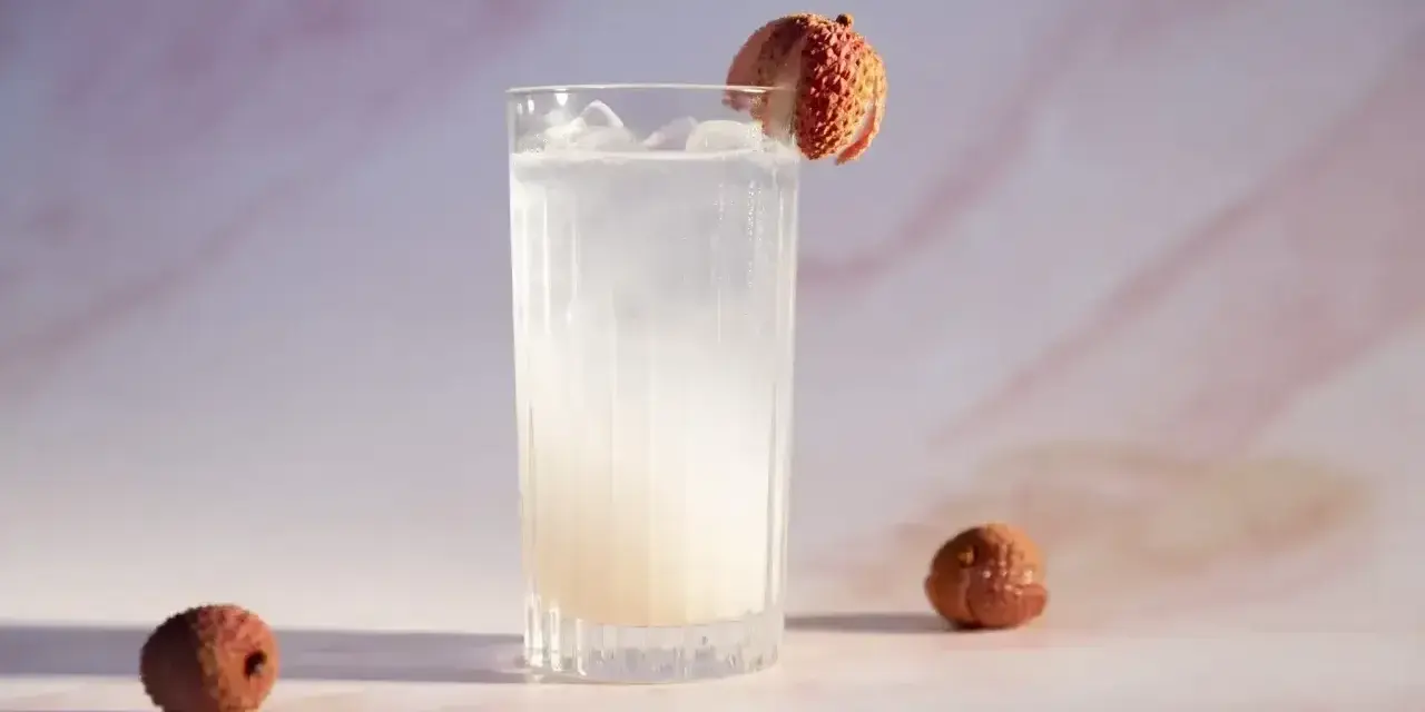 Orzeźwiający drink z liczi, ozdobiony owocem, z dwoma całymi liczi obok. Idealny na letnie popołudnie.