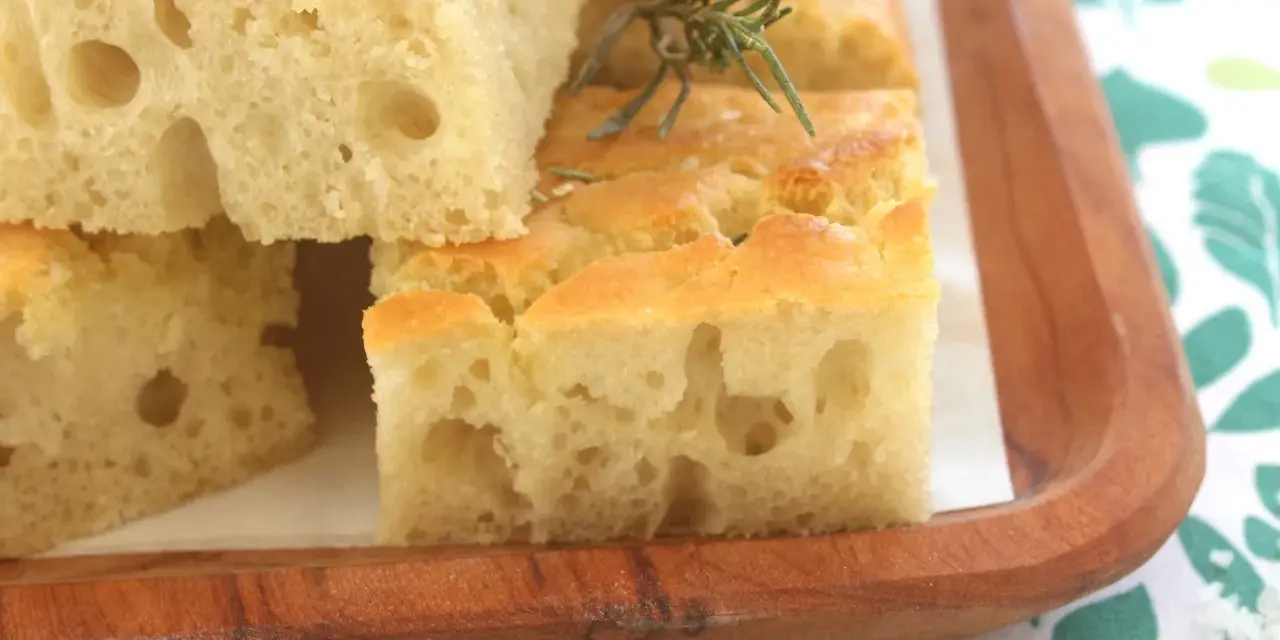 Focaccia alta e soffice, tagliata a cubetti, guarnita con rosmarino e sale grosso, servita su un tagliere di legno.