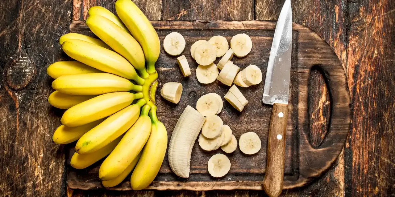 Pęczek żółtych bananów i pokrojone plasterki na desce. Dowiedz się, jak przechowywać banany, by dłużej były świeże.