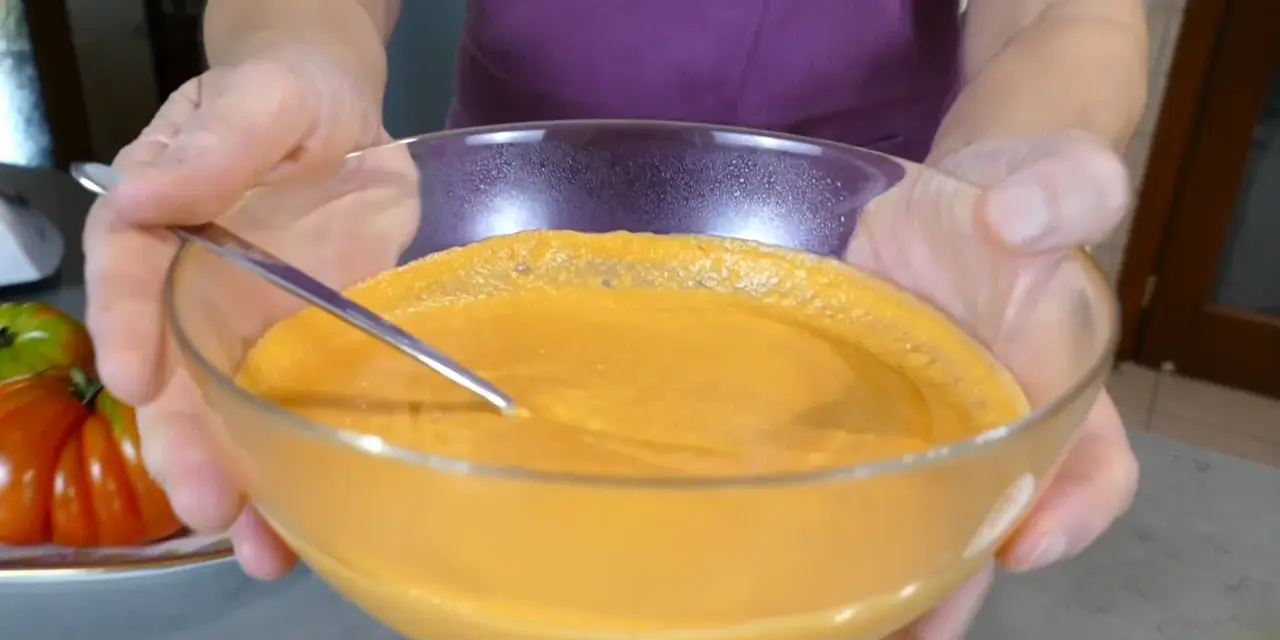 Mani che sorreggono una ciotola di vetro con una cremosa maionese di pomodoro, pronta per essere gustata.