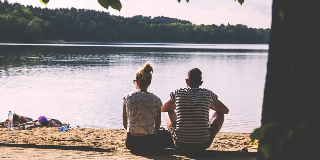 Para, siedząca na plaży, patrzy na jezioro. Idealny partner dla wagi, szukający spokoju i harmonii.