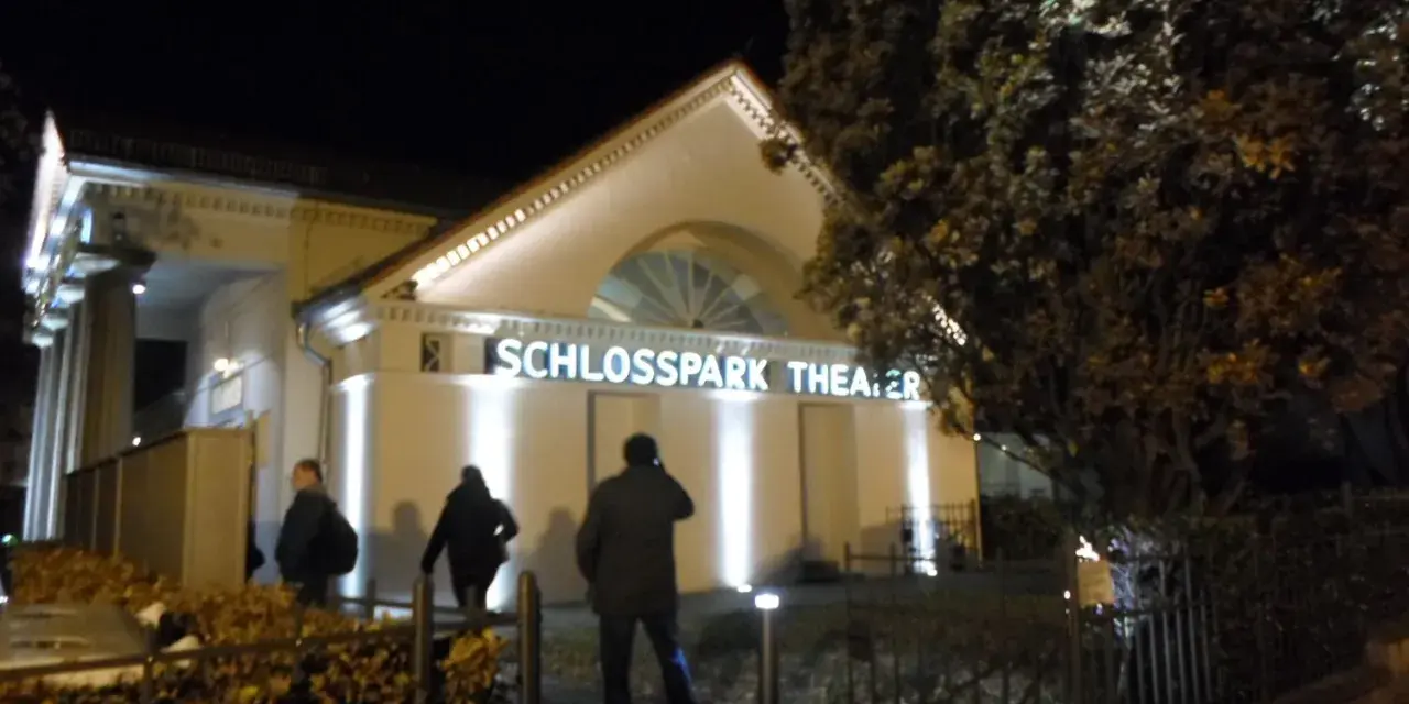 Abendliche Beleuchtung am **Schlosspark Theater**. Drei Personen nähern sich dem Eingang.
