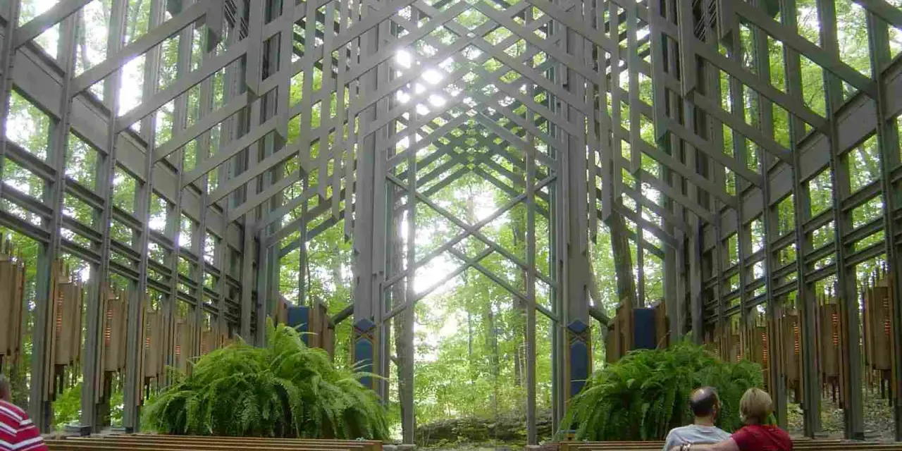 Wnętrze kaplicy w lesie, gdzie architektura organiczna łączy się z naturą. Drewniane ławki, paprocie i światło przenikające przez kratownicę tworzą spokojną atmosferę.