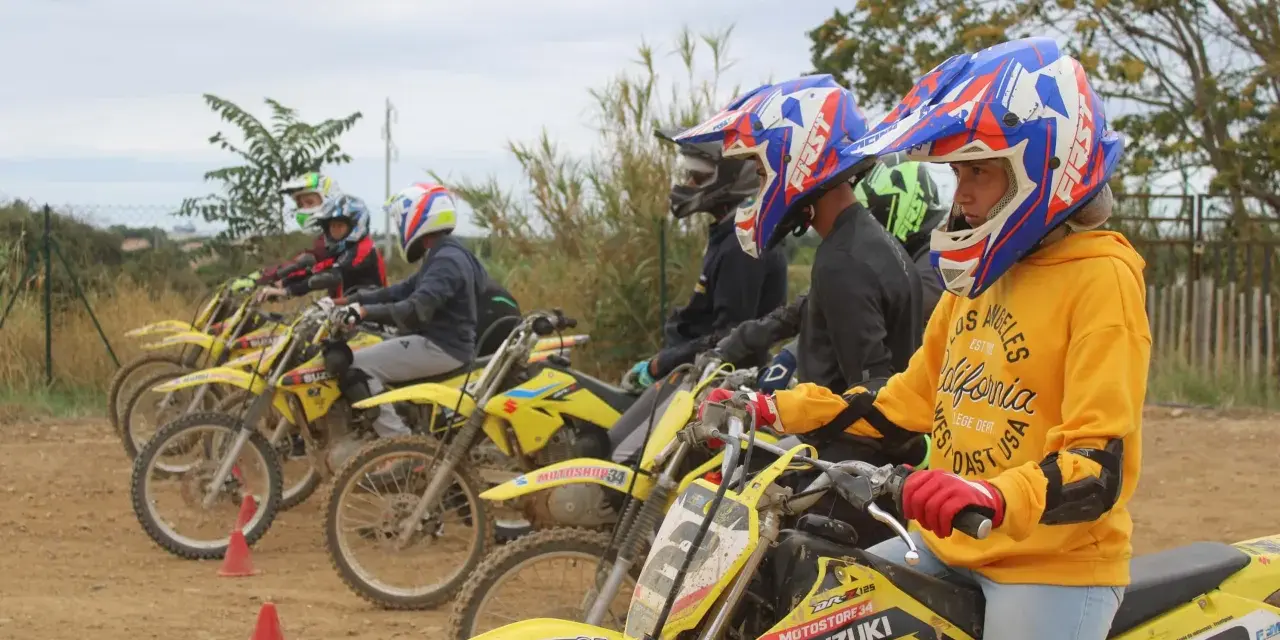 Jeunes pilotes prêts pour une course de moto cross. Casques colorés et motos jaunes alignées.