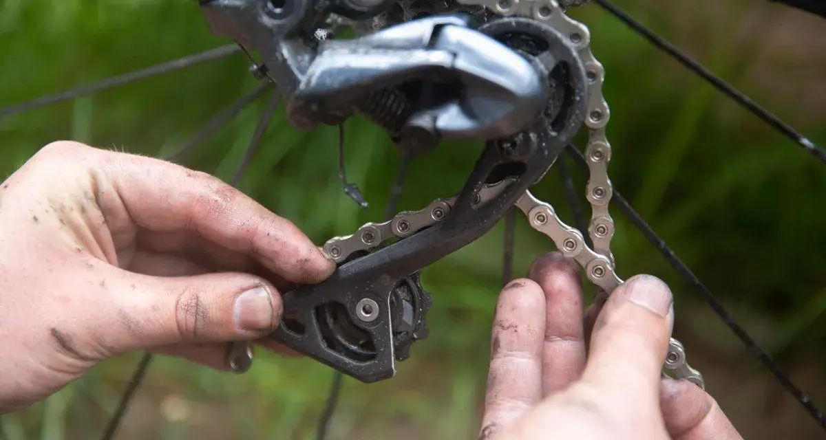 Smutsiga händer arbetar med att byta kedja på en cykel. Detaljbild på bakväxeln och kedjan.