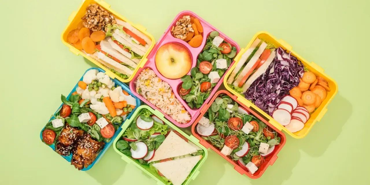 Kolorowe pojemniki na lunch z kanapkami, sałatkami, owocami i warzywami.
