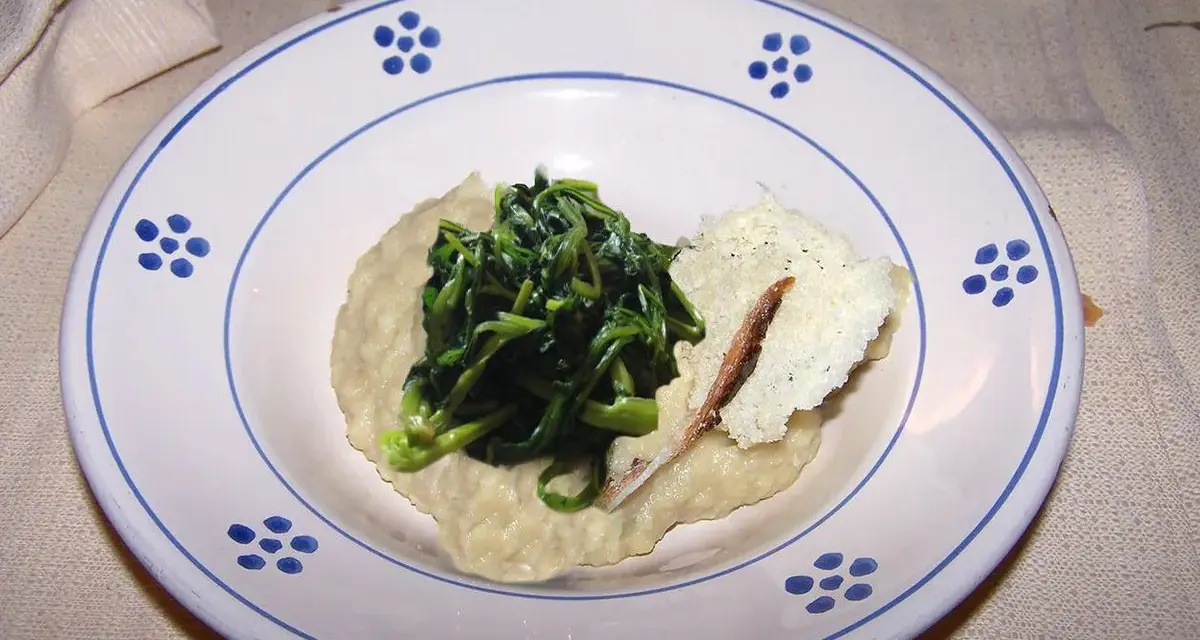 Piatto con fave e cicoria saltata, guarnito con una scaglia di formaggio e un'acciuga.