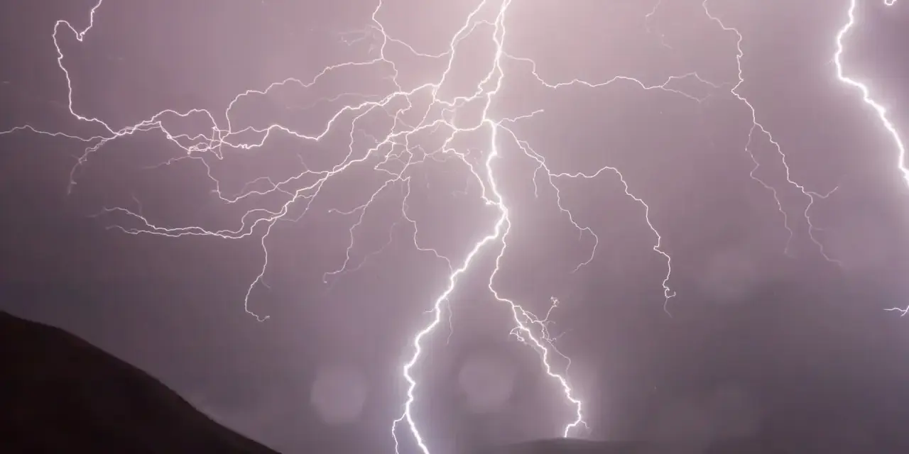 Éclairs zébrant un ciel sombre, illuminant un paysage montagneux lors d'un photo d'orage spectaculaire.