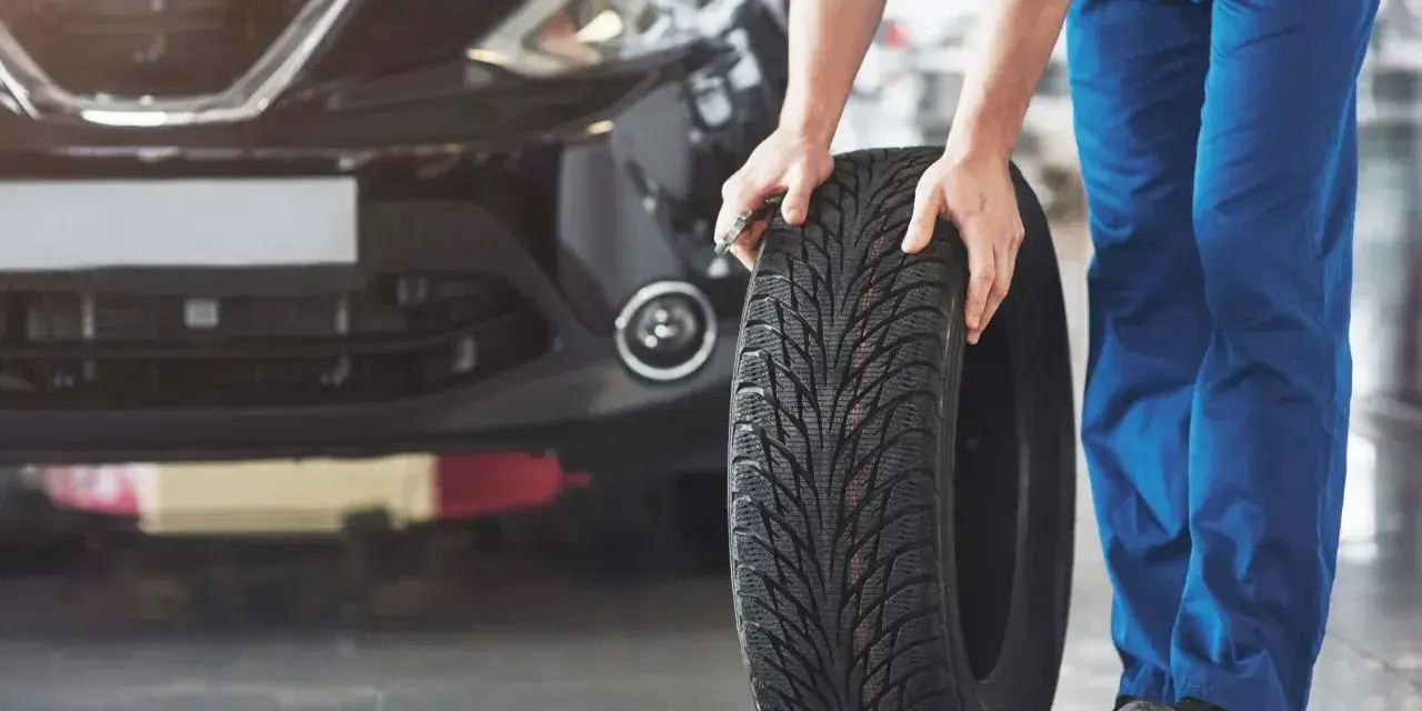 Mechanik pokazuje, jak założyć opony w dobrym kierunku. Widać bieżnik i czarne auto.