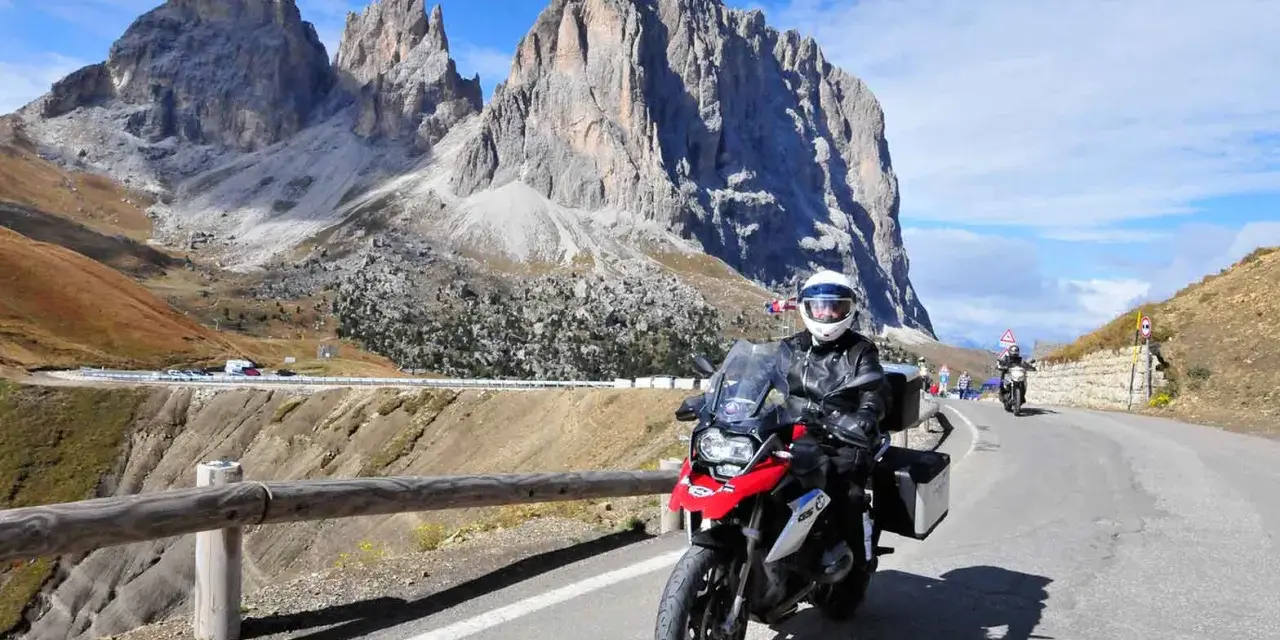 Motocyklista przemierza malowniczą drogę w Dolomitach. Pogoda dopisuje, a widoki zapierają dech w piersiach.