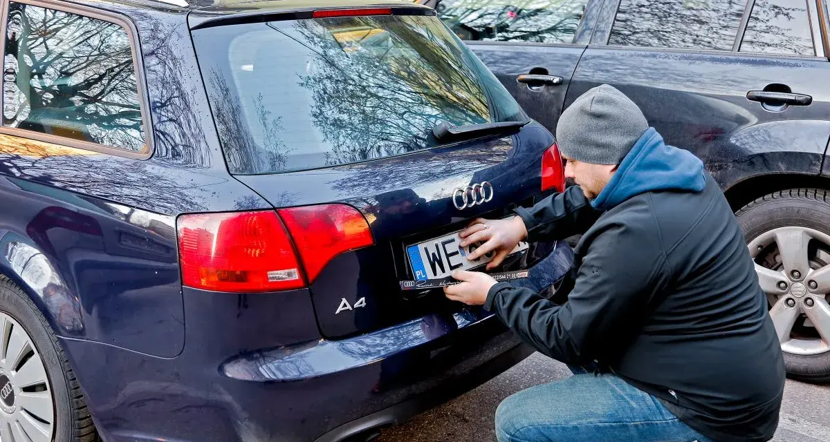 Mężczyzna montuje tablicę rejestracyjną na samochodzie Audi A4. Nowa rrs rejestracja gotowa do drogi.