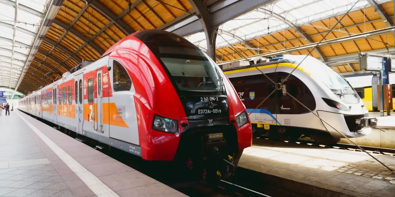 Dwa nowoczesne pociągi, czerwony i srebrny, czekają na pasażerów na dworcu. To idealny pociąg do poznania nowych miejsc.