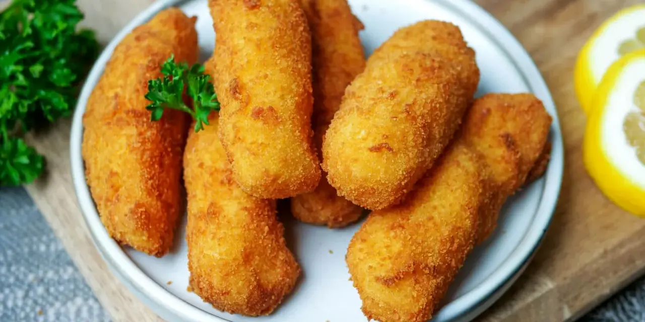 Knusprige kroketten aus kartoffelbrei, goldbraun frittiert, garniert mit Petersilie und Zitronenspalten.