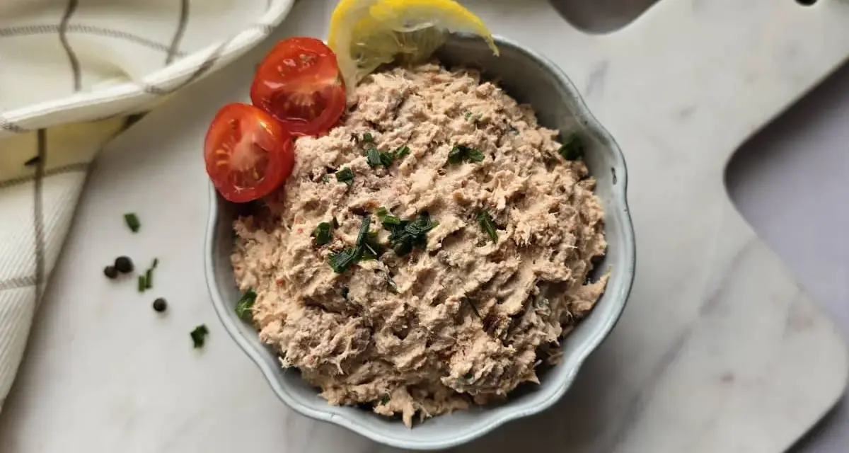 Un bol de rillettes de thon, garni de tomates cerises et de quartiers de citron, prêt à être dégusté.