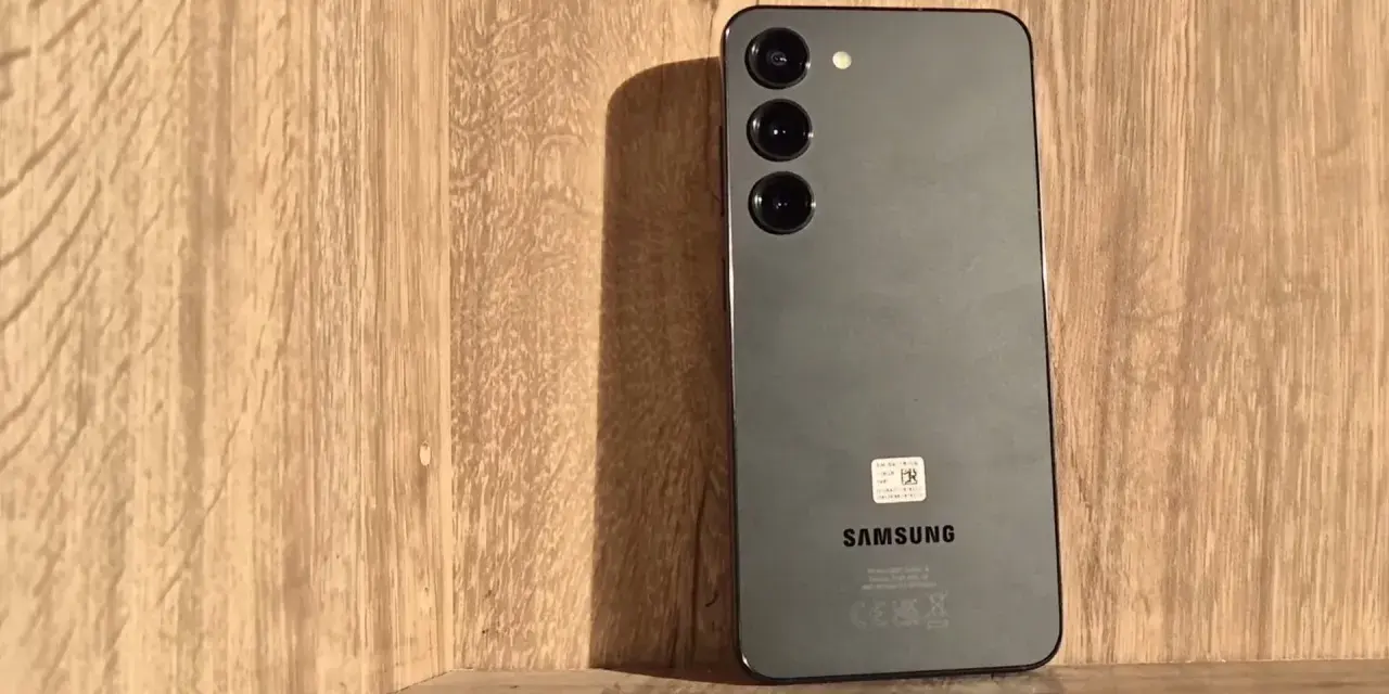 Szary Samsung S23 z trzema obiektywami aparatu na drewnianym tle. Długo działająca bateria pozwoli Ci cieszyć się nim przez cały dzień.