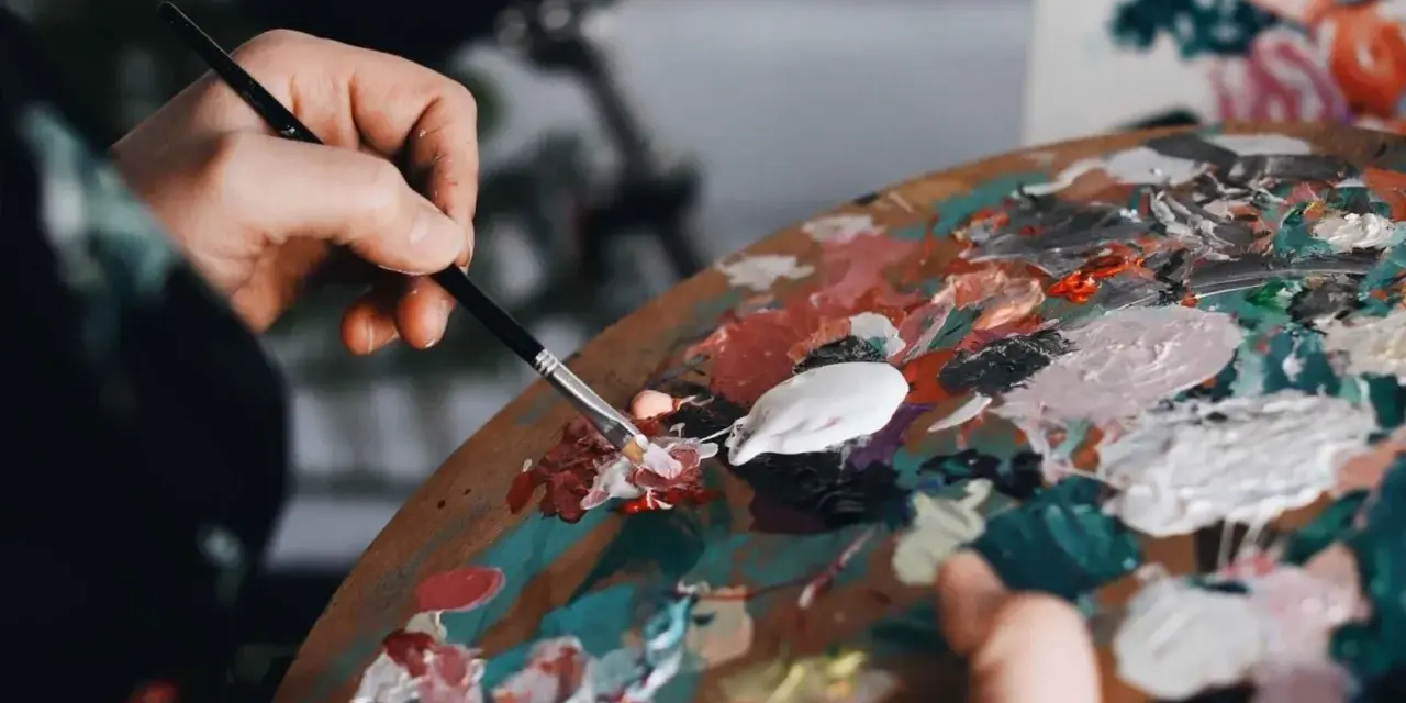 Une main mélange des couleurs vives sur une palette, prête à passer pour un peintre.