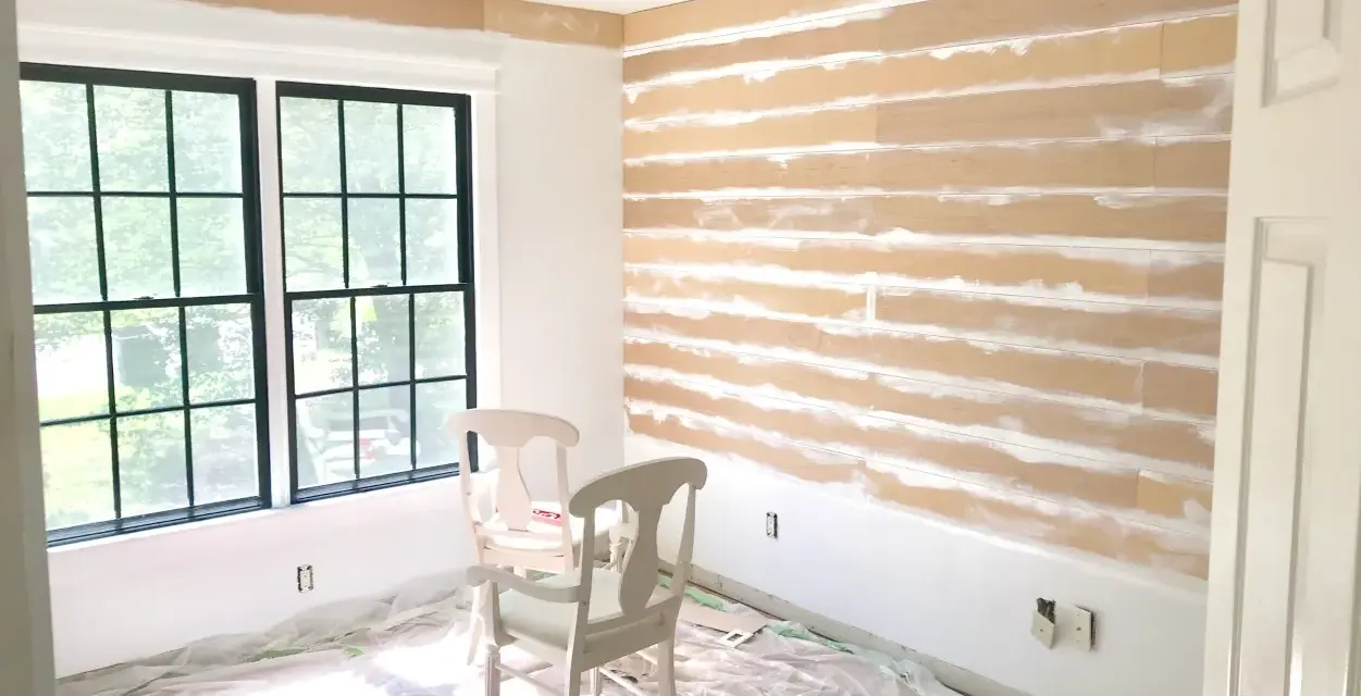 Room in progress, showing how to install shiplap on the wall. Two chairs sit on protective plastic sheeting.