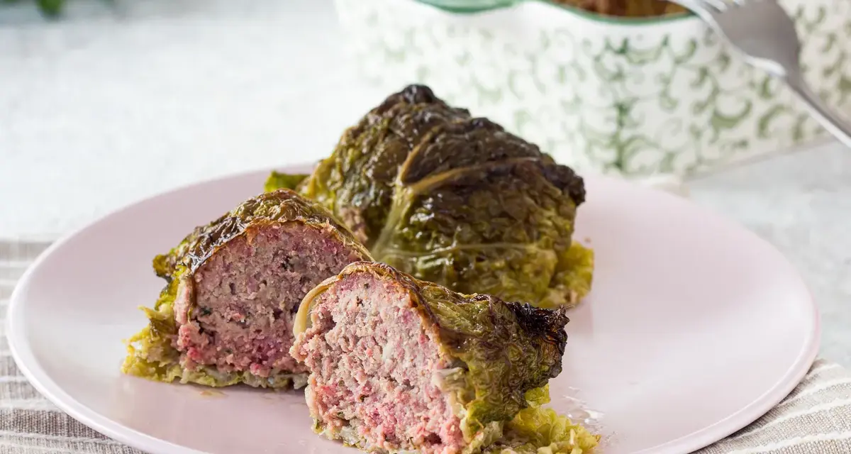 Involtini di verza con carne succulenta, uno tagliato a metà per mostrare il ripieno saporito.