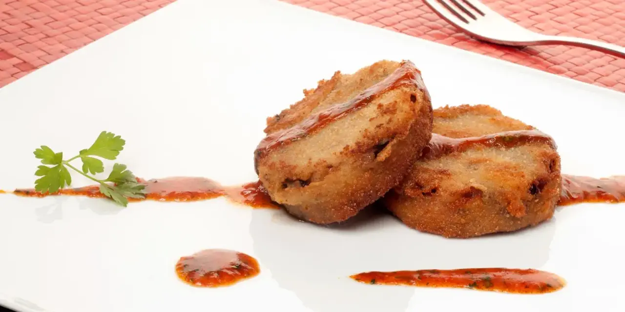 Dos manitas de cerdo rebozadas y fritas, servidas con salsa roja y perejil en un plato blanco.