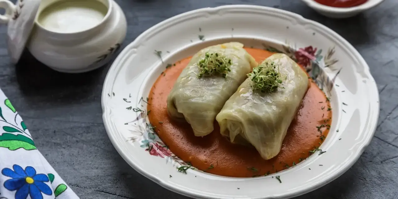 Dwa gołąbki w sosie pomidorowym, udekorowane kiełkami. Pytanie brzmi: czy gołąbki można mrozić? Obok sos śmietanowy i ketchup.