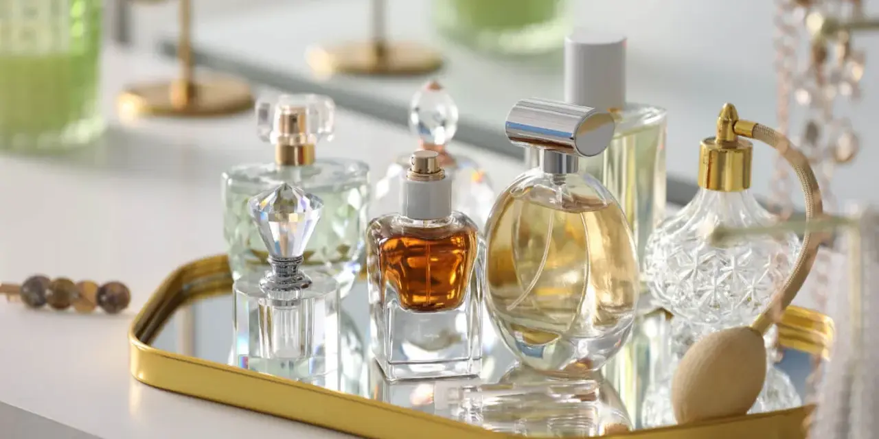 Kolekcja flakonów z płynną esencją perfum, w tym jeden z atomizerem, na złotym lustrzanym tacy.