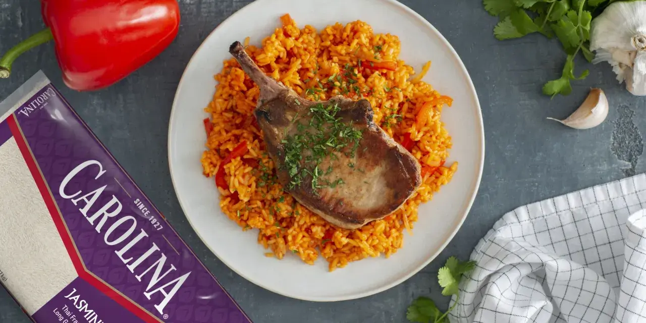 Chuleta de cerdo jugosa sobre arroz rojo con pimientos.