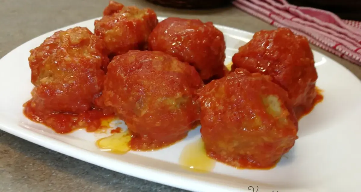 Polpette di pane al sugo, morbide e saporite, servite su un piatto bianco. Un classico della cucina italiana.