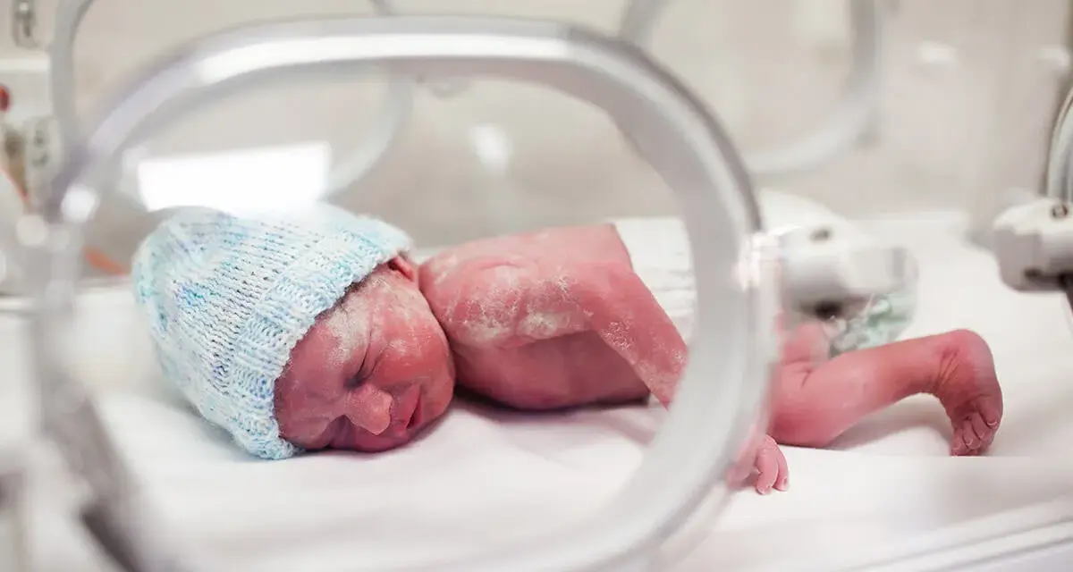 Maleńki noworodek, dziecko urodzone w 20 tygodniu ciąży, w inkubatorze, w niebieskiej czapeczce.
