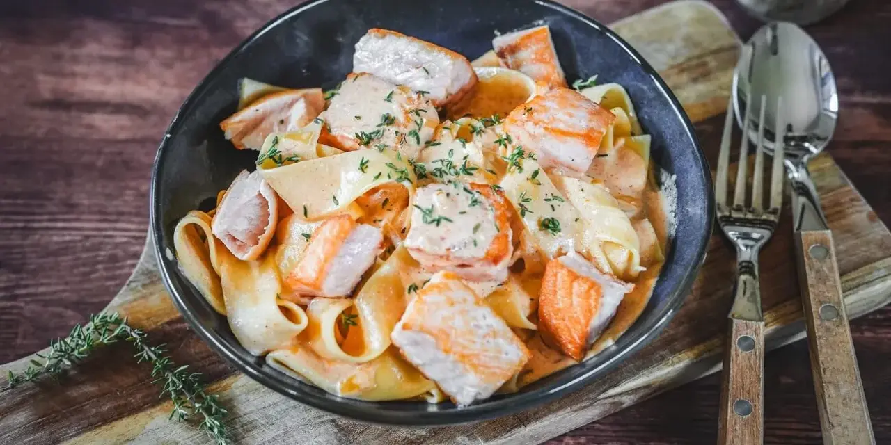 Breite Bandnudeln mit saftigen Lachs-Stücken in cremiger Lachs Sahne Sauce, garniert mit frischen Kräutern. Ein Genuss!