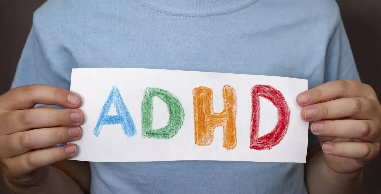 Mani di bambino tengono un foglio con la scritta "ADHD" colorata. Riconoscere i sintomi dell'ADHD è il primo passo.