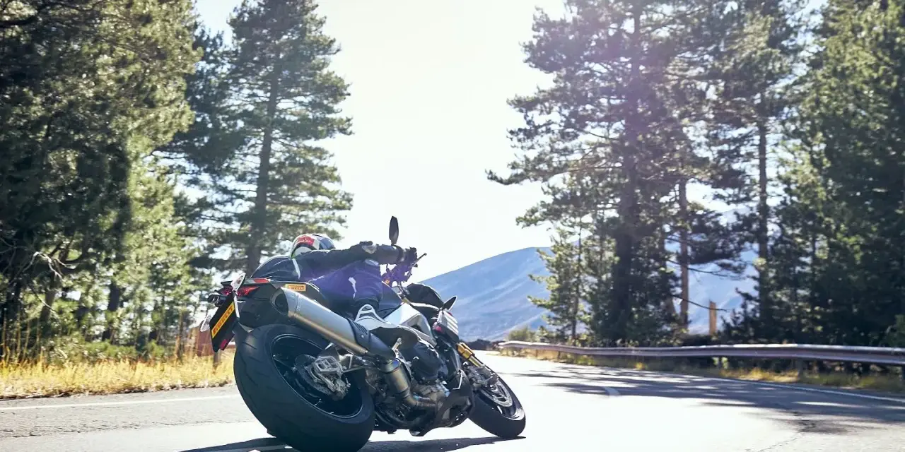 Motocyklista na zakręcie, otoczony lasem, z dumą prezentuje opony Pirelli. Jazda w stylu Pirelli klub.
