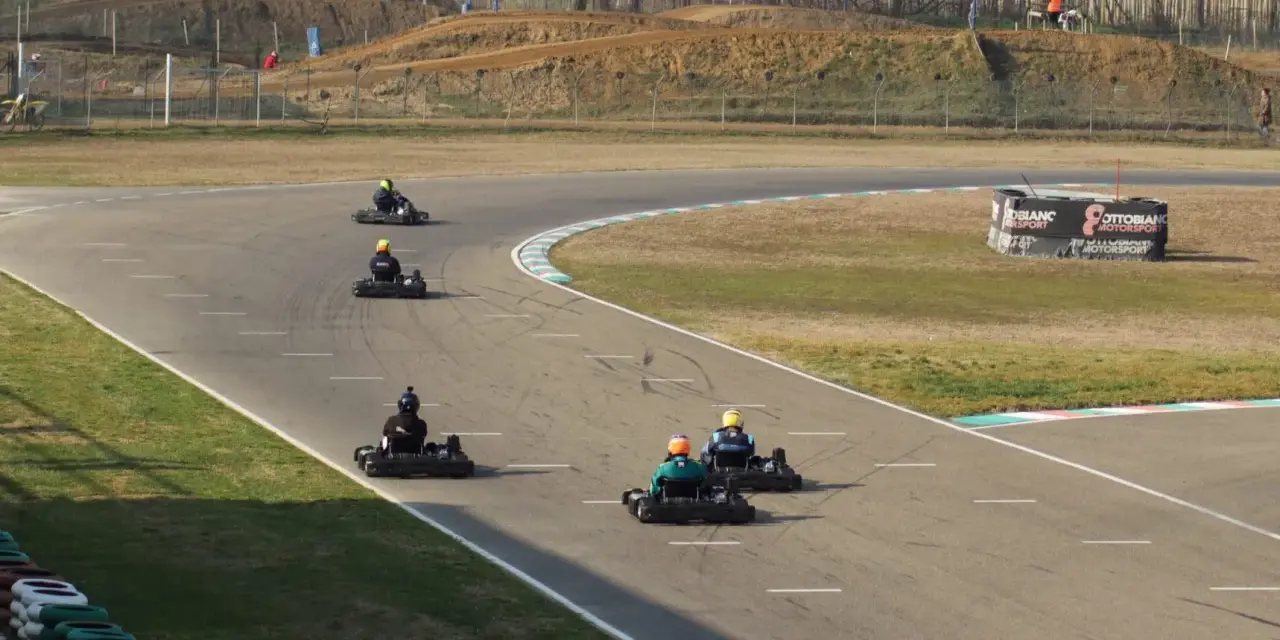 Gara di go-kart su pista con piloti in azione. Sullo sfondo, un cartellone pubblicitario con la scritta "Ottobiano Motorsport".