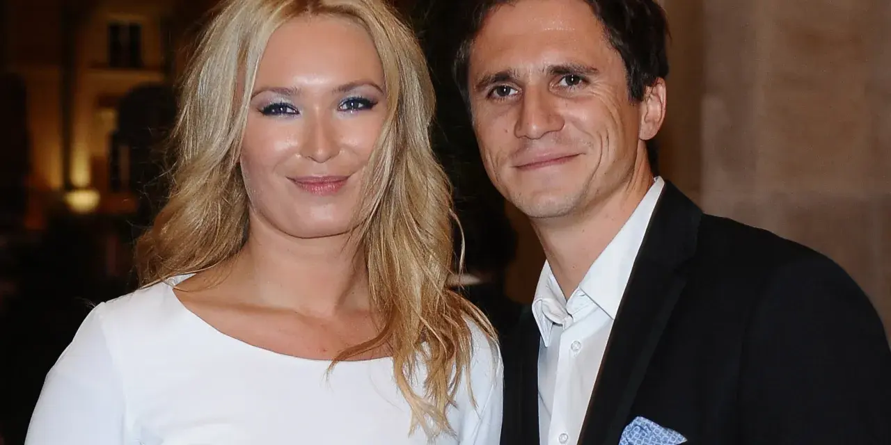 Uśmiechnięta para, być może rodzice Sambora Czarnoty, pozuje do zdjęcia. Kobieta ma blond włosy i białą sukienkę, mężczyzna czarny garnitur.