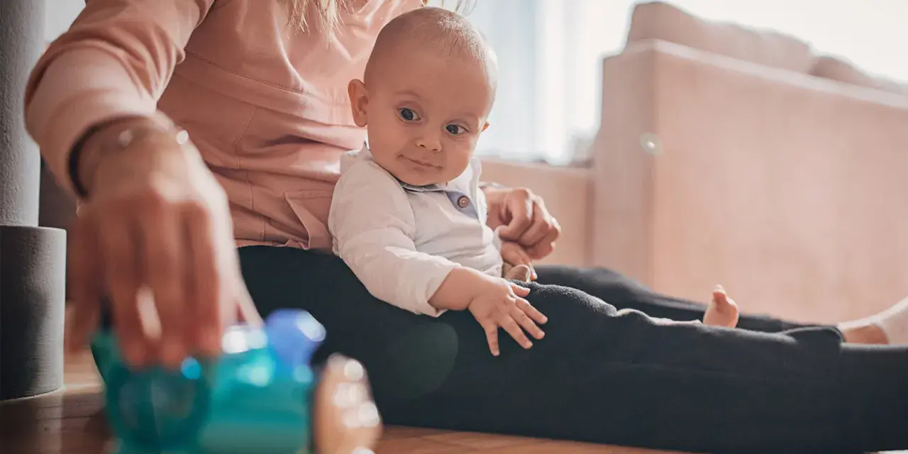 Mama bawi się z 9-miesięcznym dzieckiem, podając mu kolorową zabawkę-pociąg.