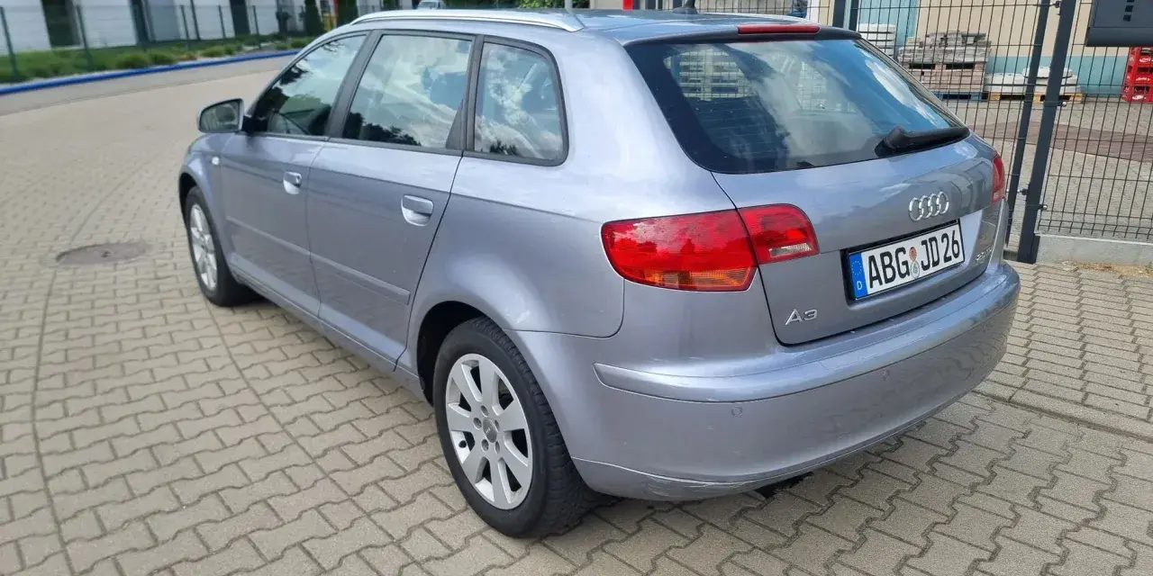Srebrny Audi A3 kombi zaparkowany na kostce brukowej, w tle domy i drzewa.