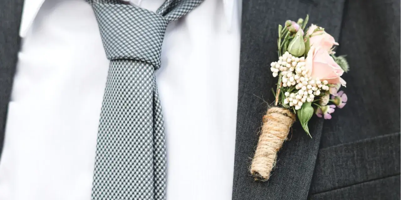 Elegancki krawat do ślubu w kratkę, biała koszula i butonierka z różową różą.