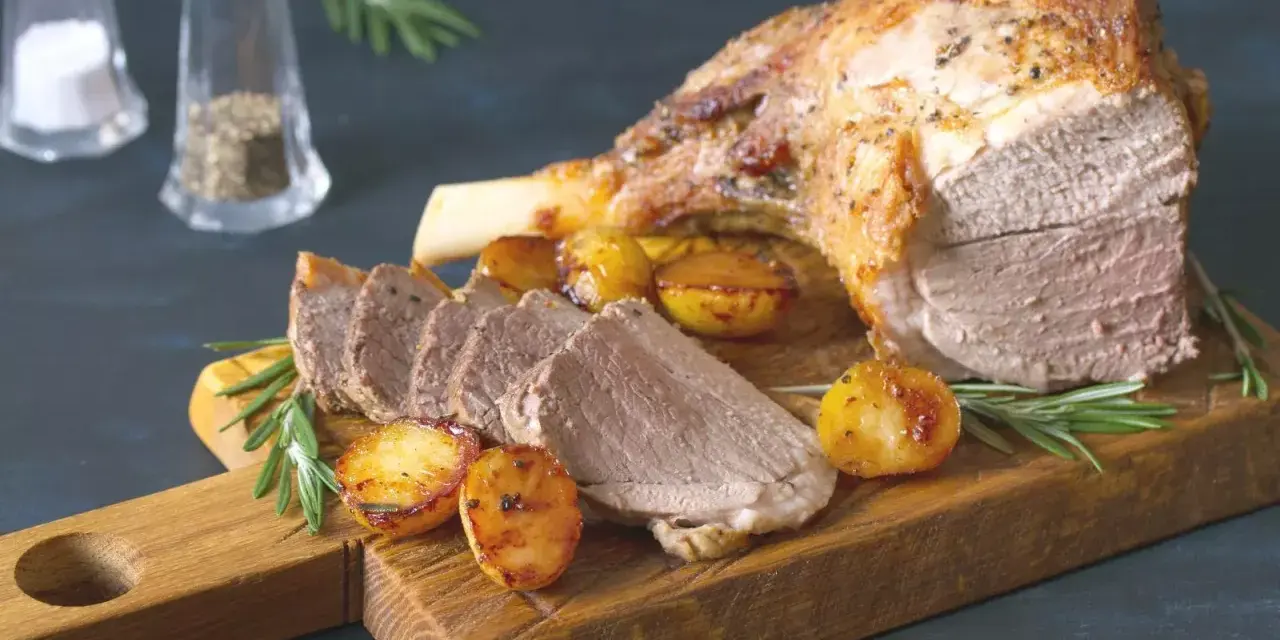 Un gigot de 7 heures, tendre et juteux, servi avec des pommes de terre rôties et du romarin sur une planche en bois.