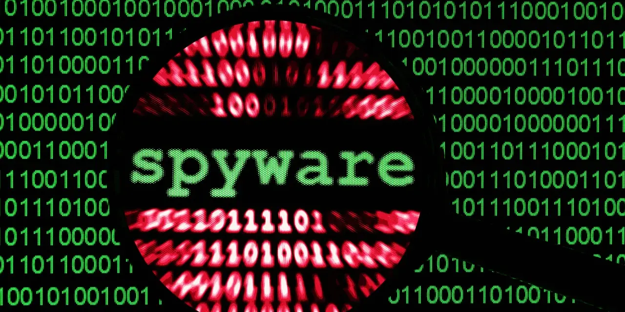 Lupa sobre código binario verde y rojo, con la palabra "spyware" en verde en el centro.