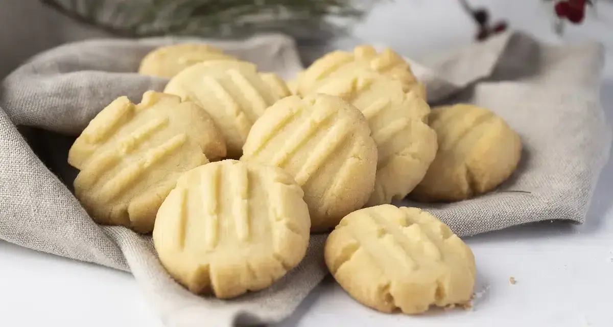 Montón de galletas de mantequilla doradas con líneas marcadas, servidas sobre una tela gris.