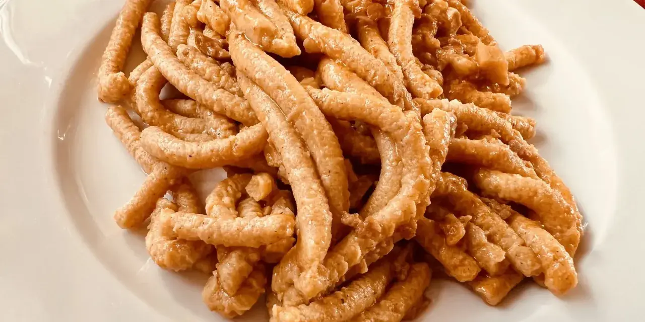 Pici all'aglione, uno dei piatti tipici di Arezzo, serviti su un piatto bianco.