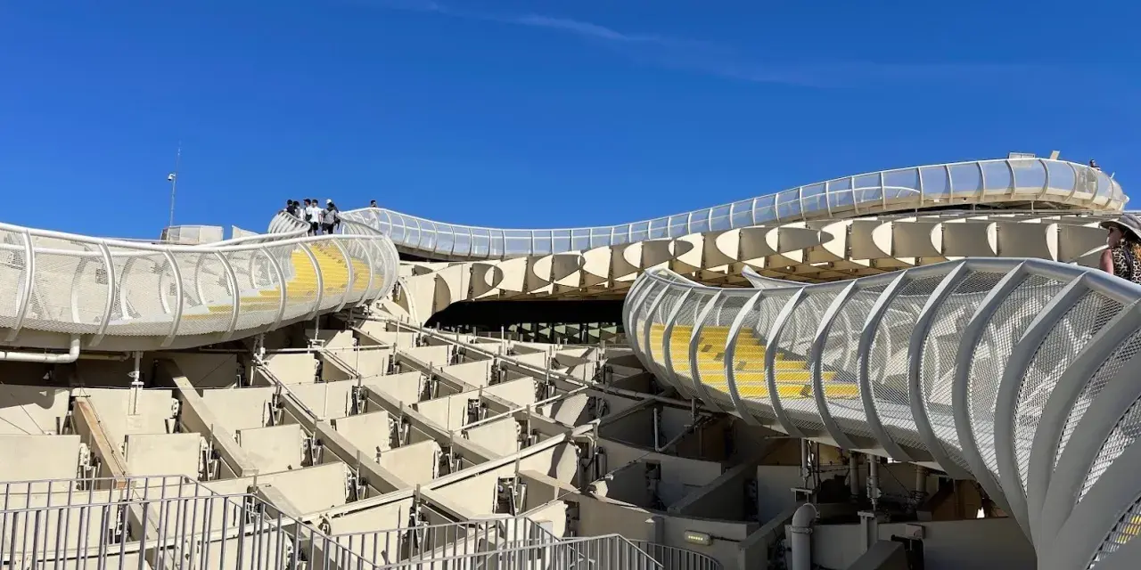 The Metropol Parasol, known as Las Setas de Sevilla, features a modern wooden structure with winding walkways and yellow steps under a clear blue sky.