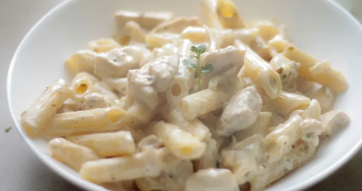 Penne z kurczakiem w kremowym sosie, udekorowane gałązką ziół. Pyszne danie, które zachwyci każdego smakosza.