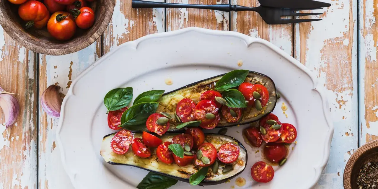 Melanzane ripiene vegetariane con pomodorini, basilico e semi di zucca, un piatto colorato e saporito.