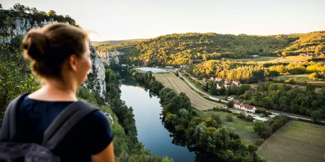 Une femme admire un paysage de carte postale lors de son voyage découverte en France. La rivière serpente à travers des collines verdoyantes et des villages pittoresques.